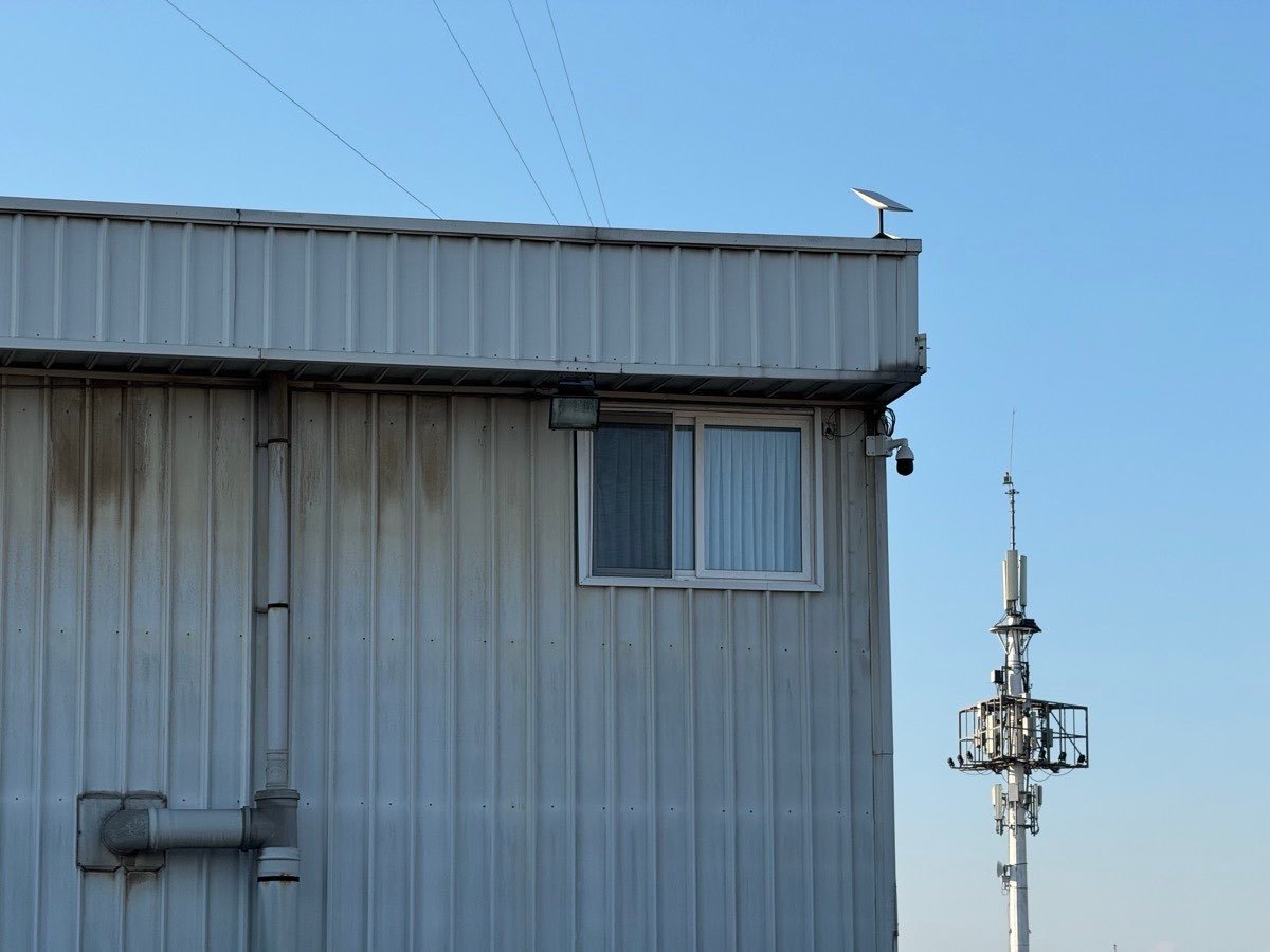Cámara PTZ montada en la esquina de una nave industrial, con torre de antenas al fondo
