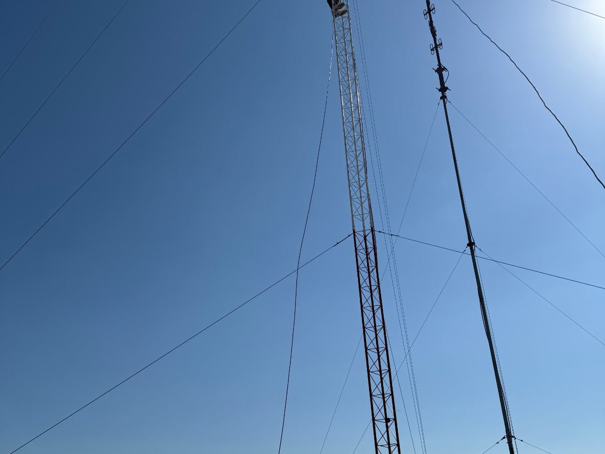 Torre de celosía y mástil con antenas direccionales y sus vientos, vistos desde abajo contra el cielo